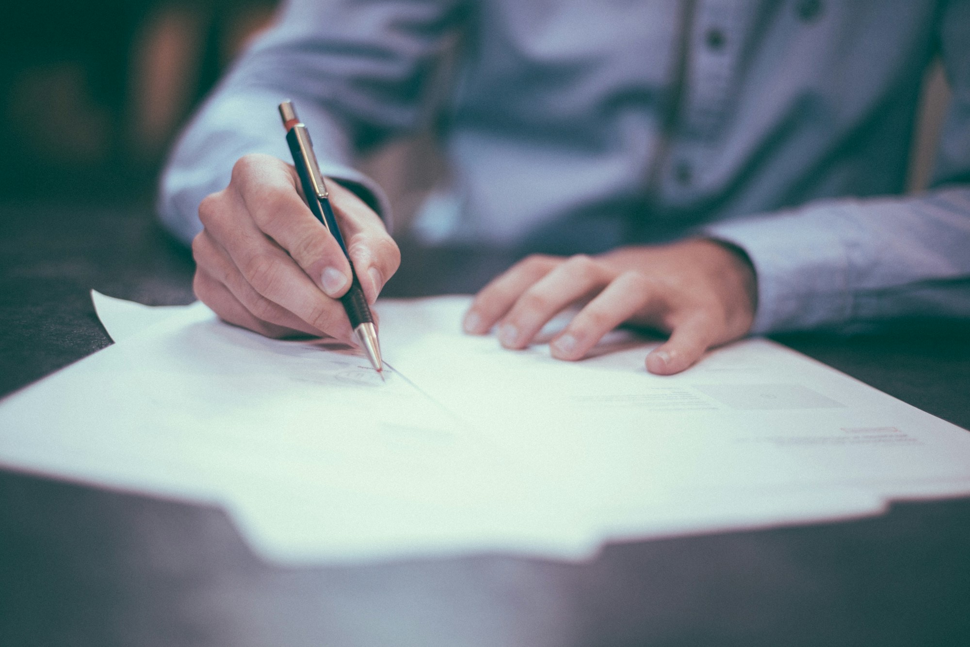 Hands signing a document with a pen